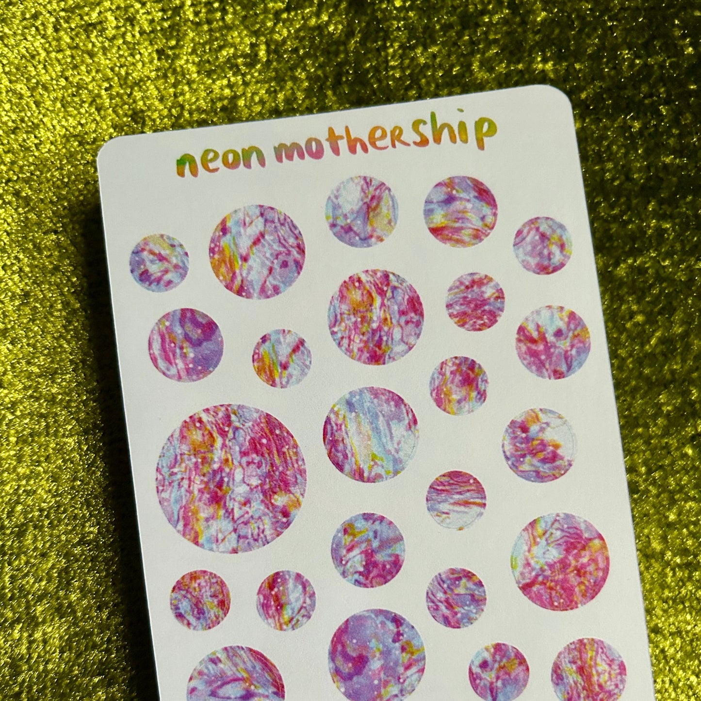 Sheet of colorful round stickers with 'neon mothership' branding on a textured green background.