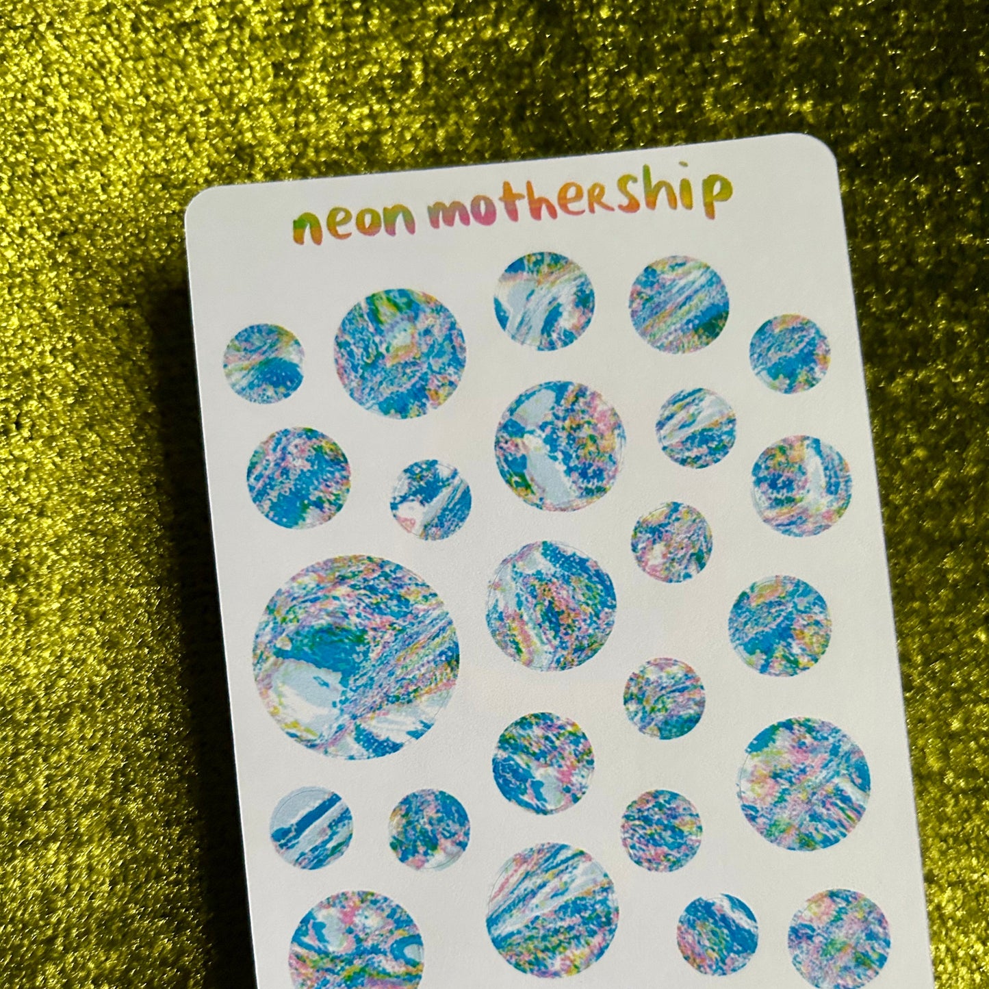 Sheet of colorful round stickers with 'neon mothership' branding on a green textured background.