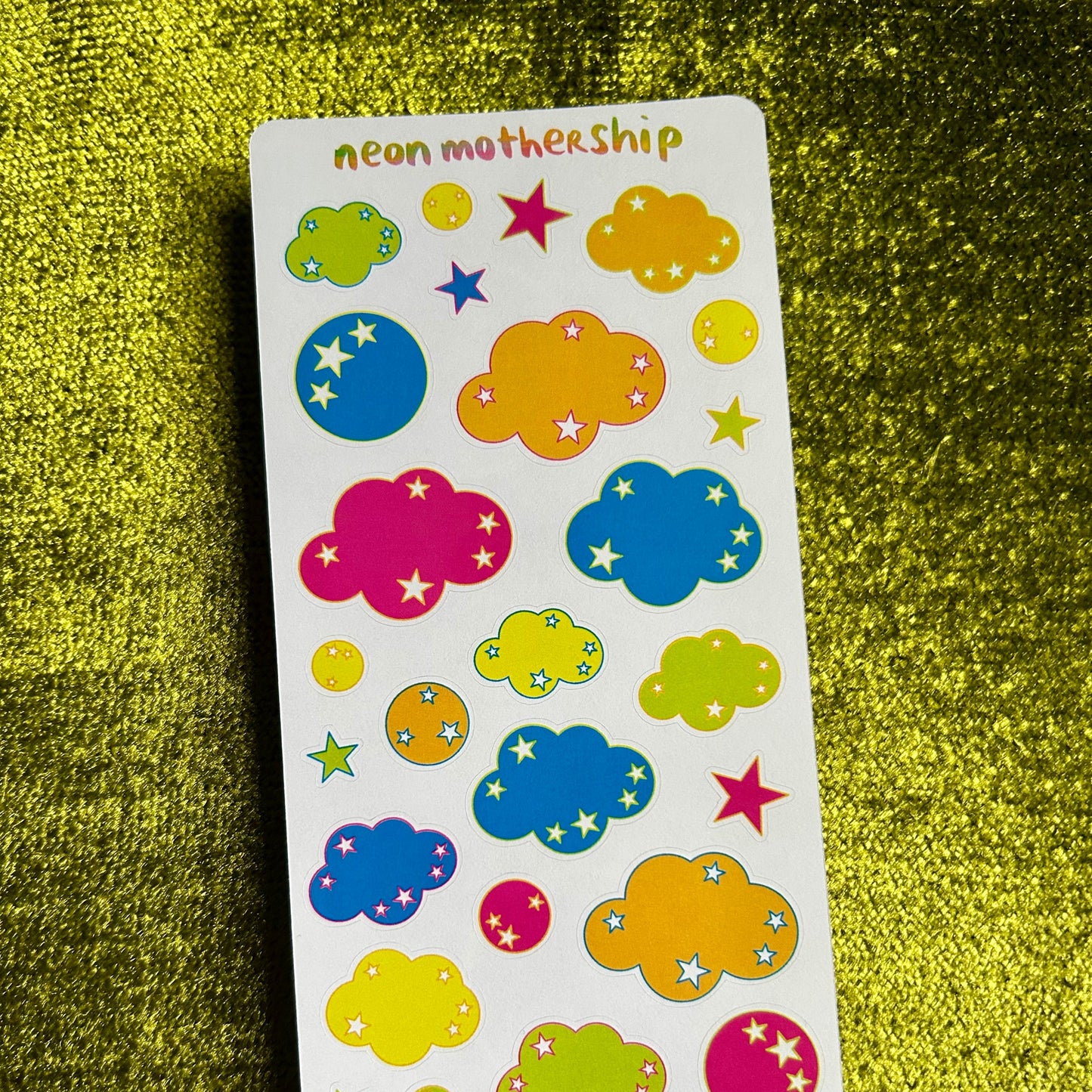Sheet of colorful cloud and star stickers on a green textured surface
