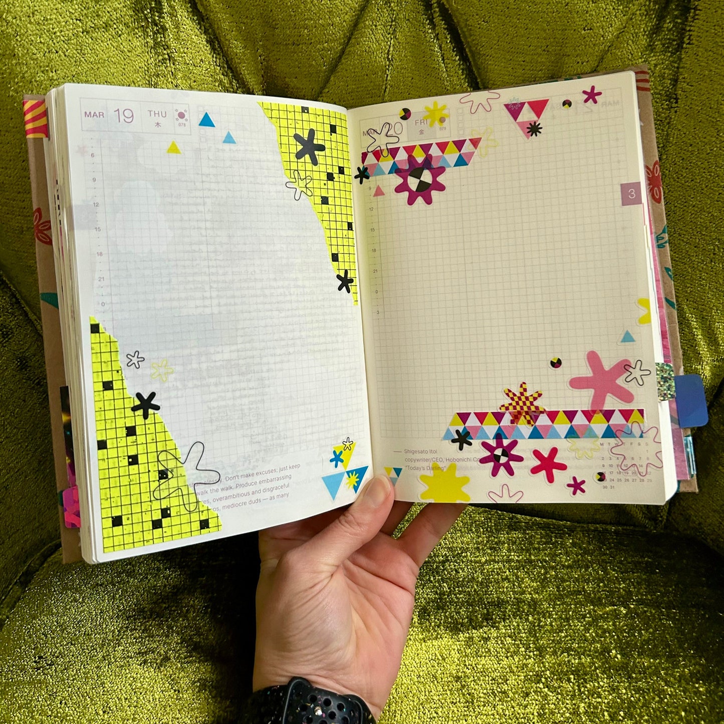 Open notebook with colorful designs held by a hand on a green textured surface