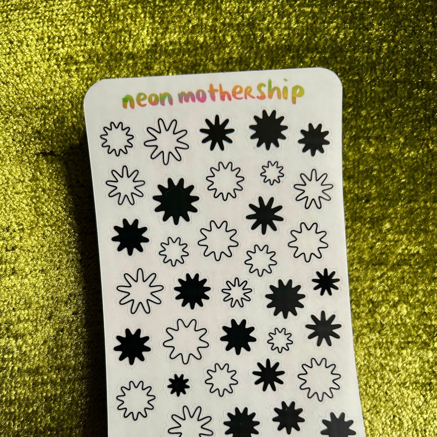 Sheet of black star-shaped stickers on a sticker sheet with 'neon mothership' branding, against a green textured background.