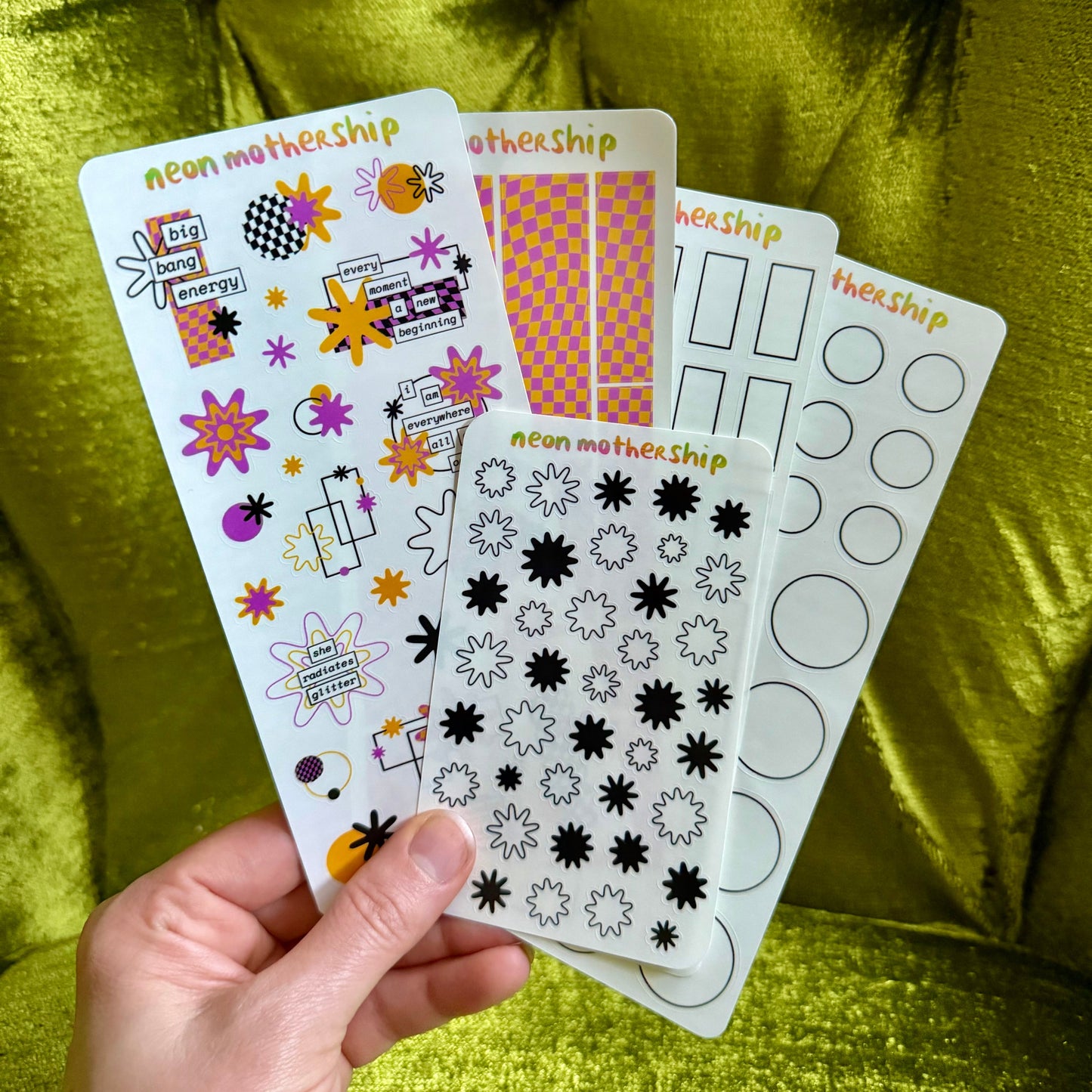 Hand holding a sheet of decorative stickers with various designs on a green fabric background