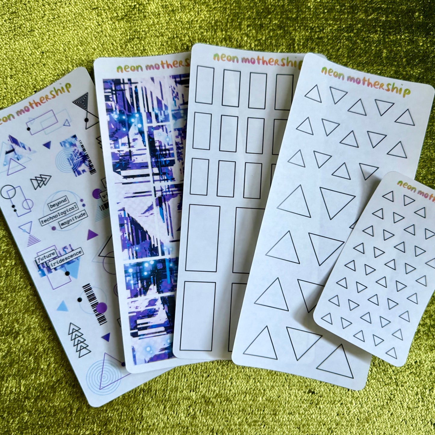 five sheets of geometric patterned stickers on a green textured surface