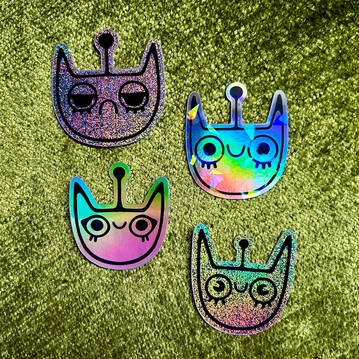 Four colorful space cat shaped stickers on a green glittery background