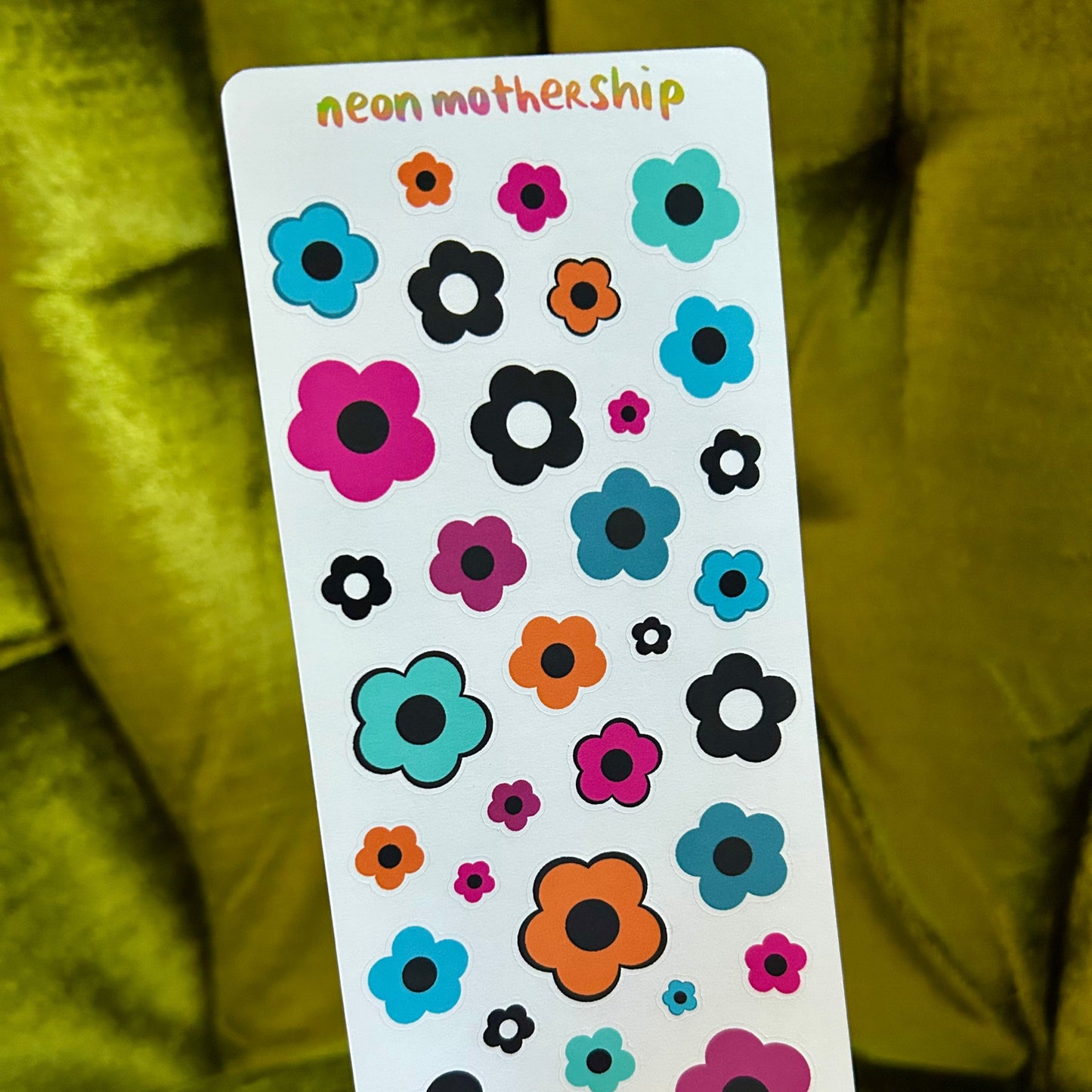 Card with colorful flower stickers held by a hand against a green fabric background