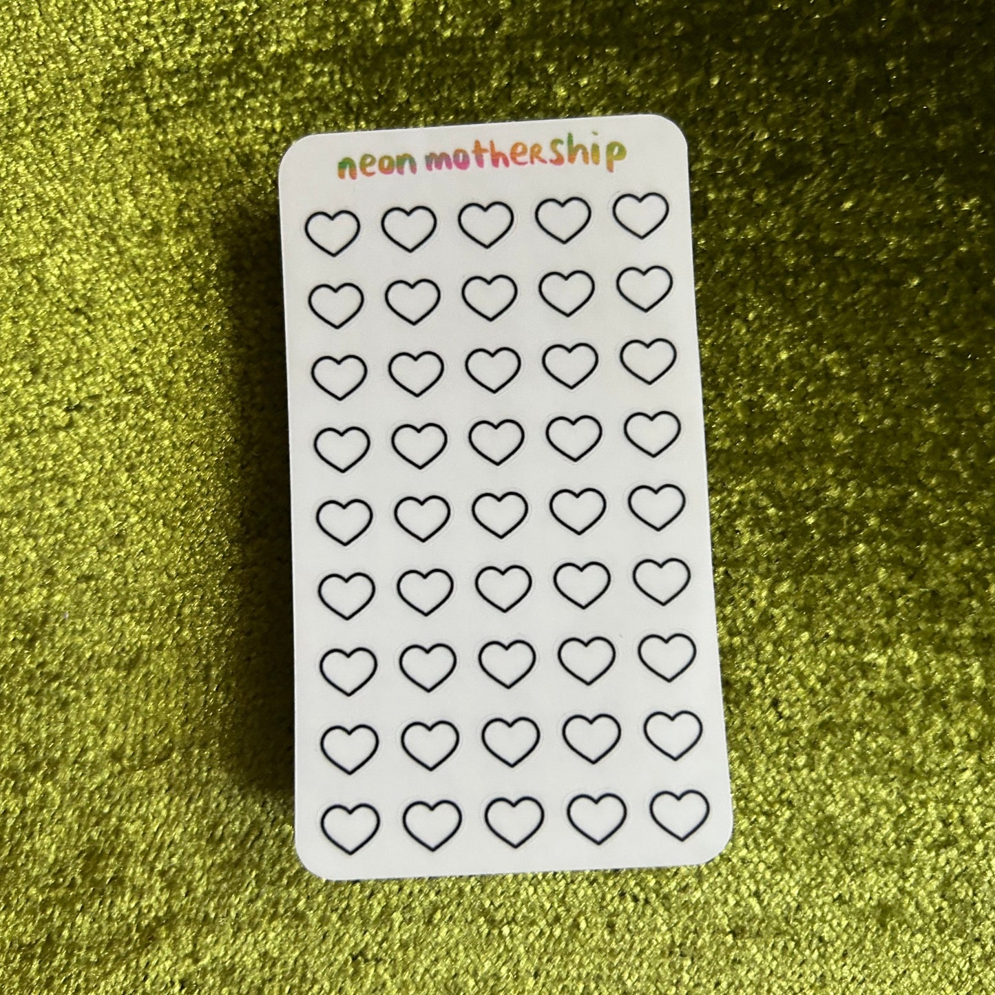 Sheet of heart-shaped stickers with 'neon mothership' branding on a green textured background
