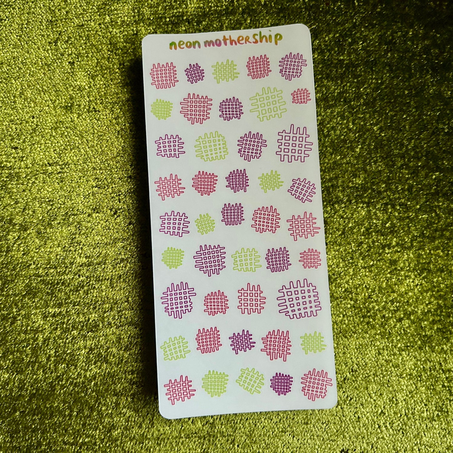 Sheet of decorative stickers with pink and green designs on a green textured surface