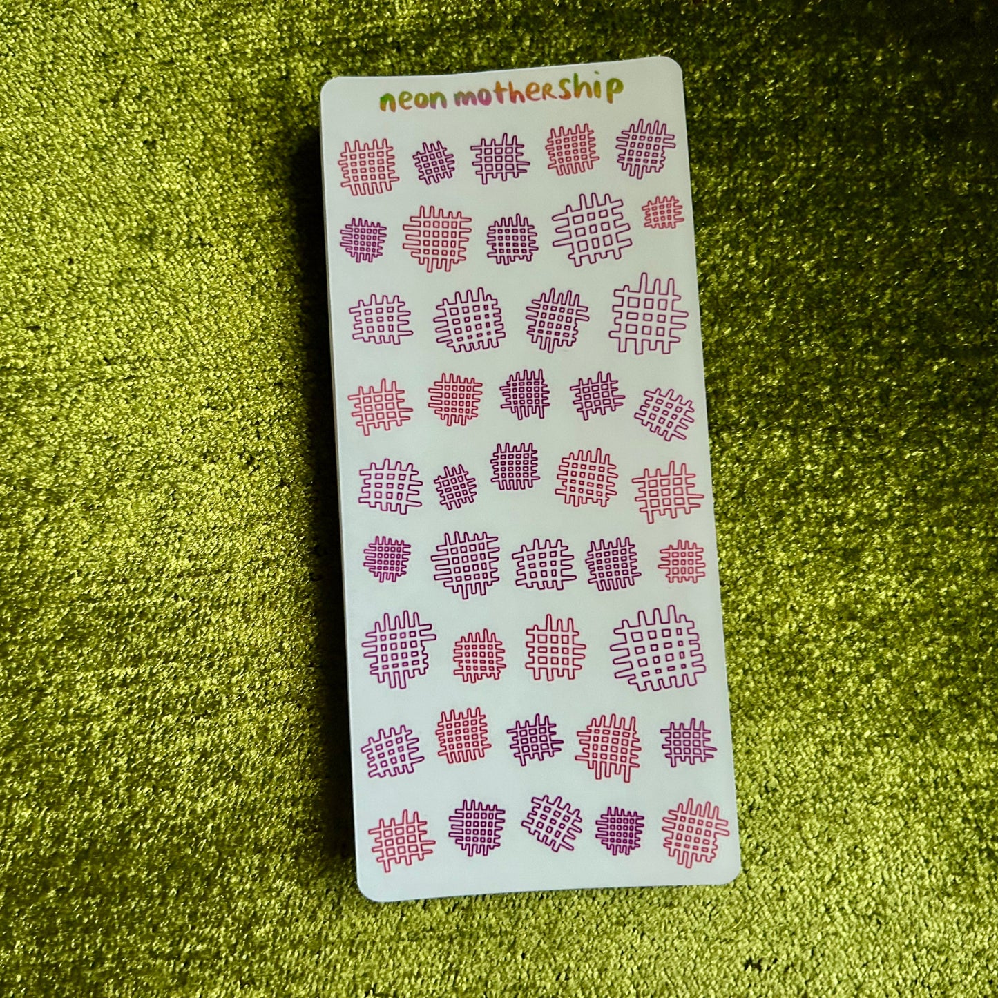 Sheet of pink and white patterned stickers on a green textured surface