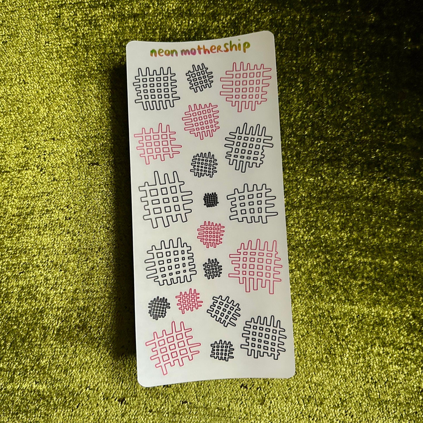 Sheet of patterned stickers with '#neon mothership' text on a green textured surface