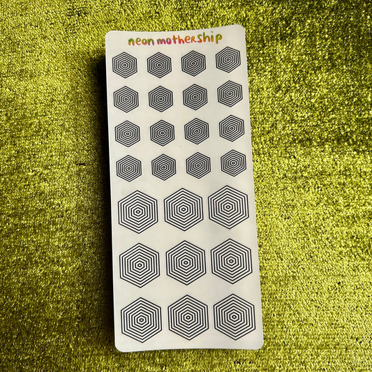 Sheet of black hexagonal stickers on a white sticker sheet with 'neon mothership' branding, placed on a green textured surface.