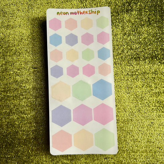 Sheet of hexagonal stickers with pastel colors on a green textured background