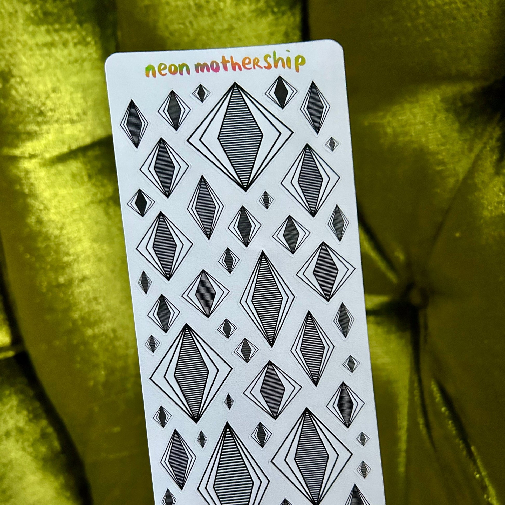 Sticker sheet with geometric diamond pattern held by a hand against a green fabric background