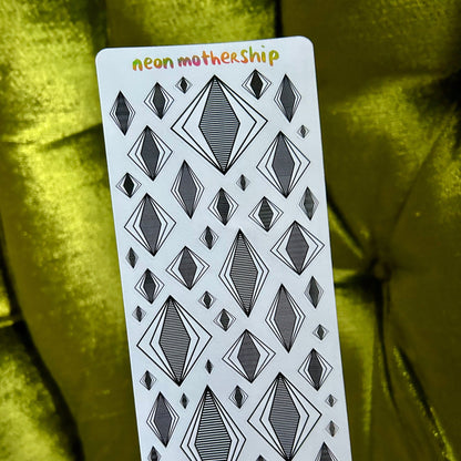 Sticker sheet with geometric diamond pattern held by a hand against a green fabric background