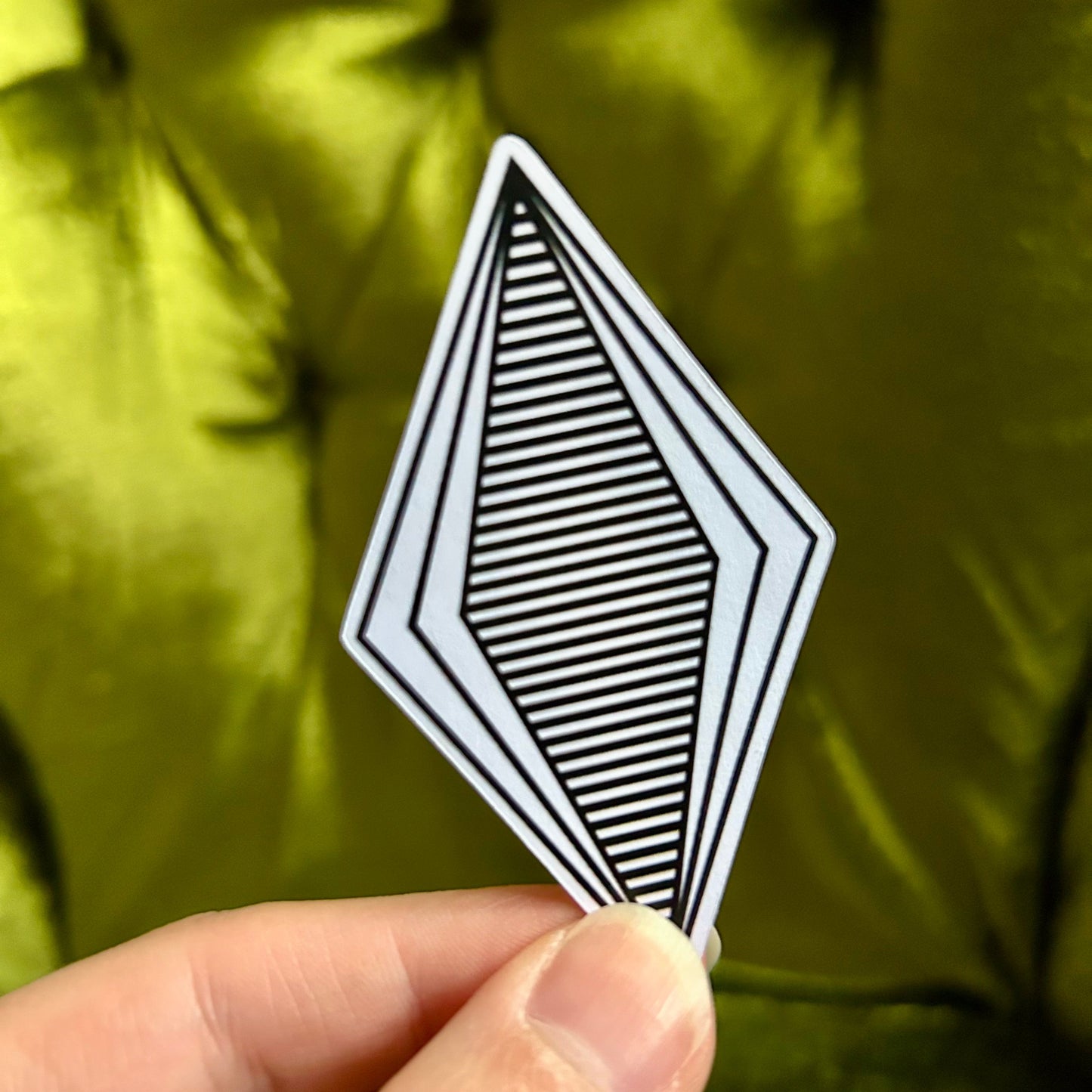 Hand holding a black and white geometric card against a green background