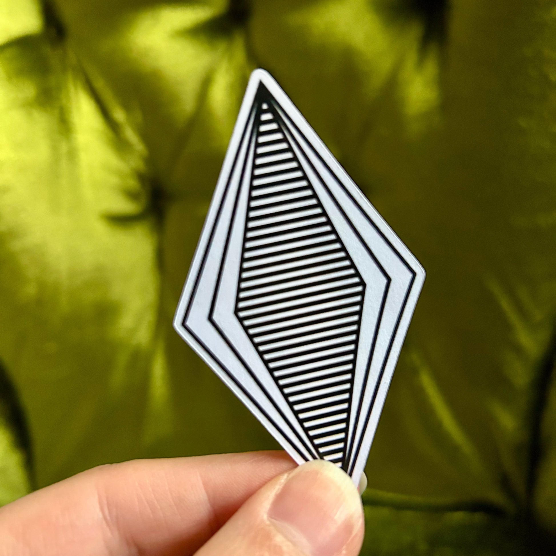 Hand holding a black and white geometric card against a green background