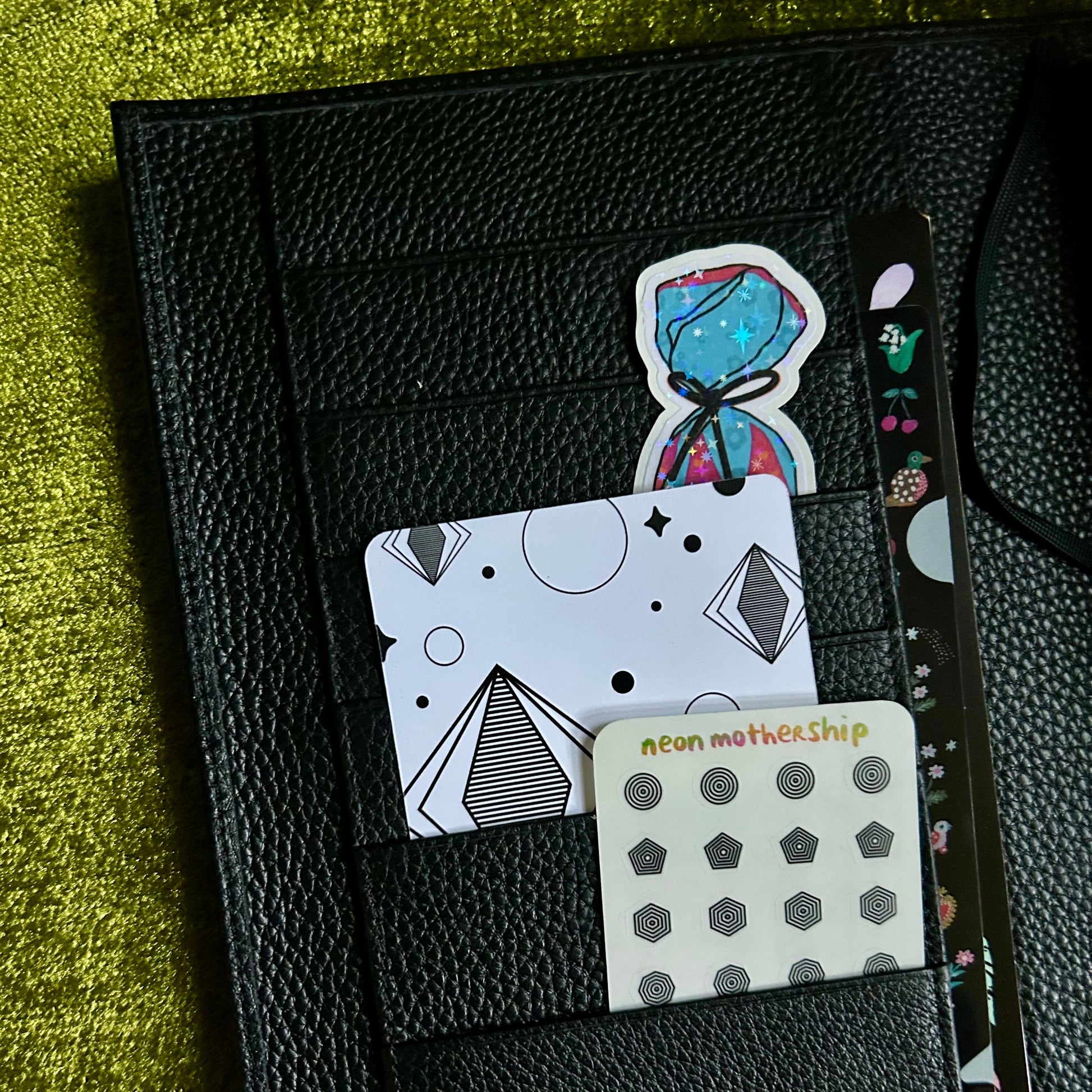 Black leather planner with card slots and a small card on a green textured surface