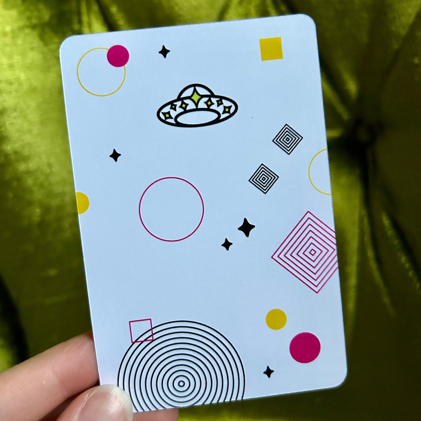 Card with geometric patterns held by a hand against a green fabric background