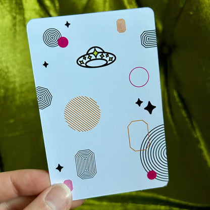 Card with geometric patterns held by a hand against a green fabric background