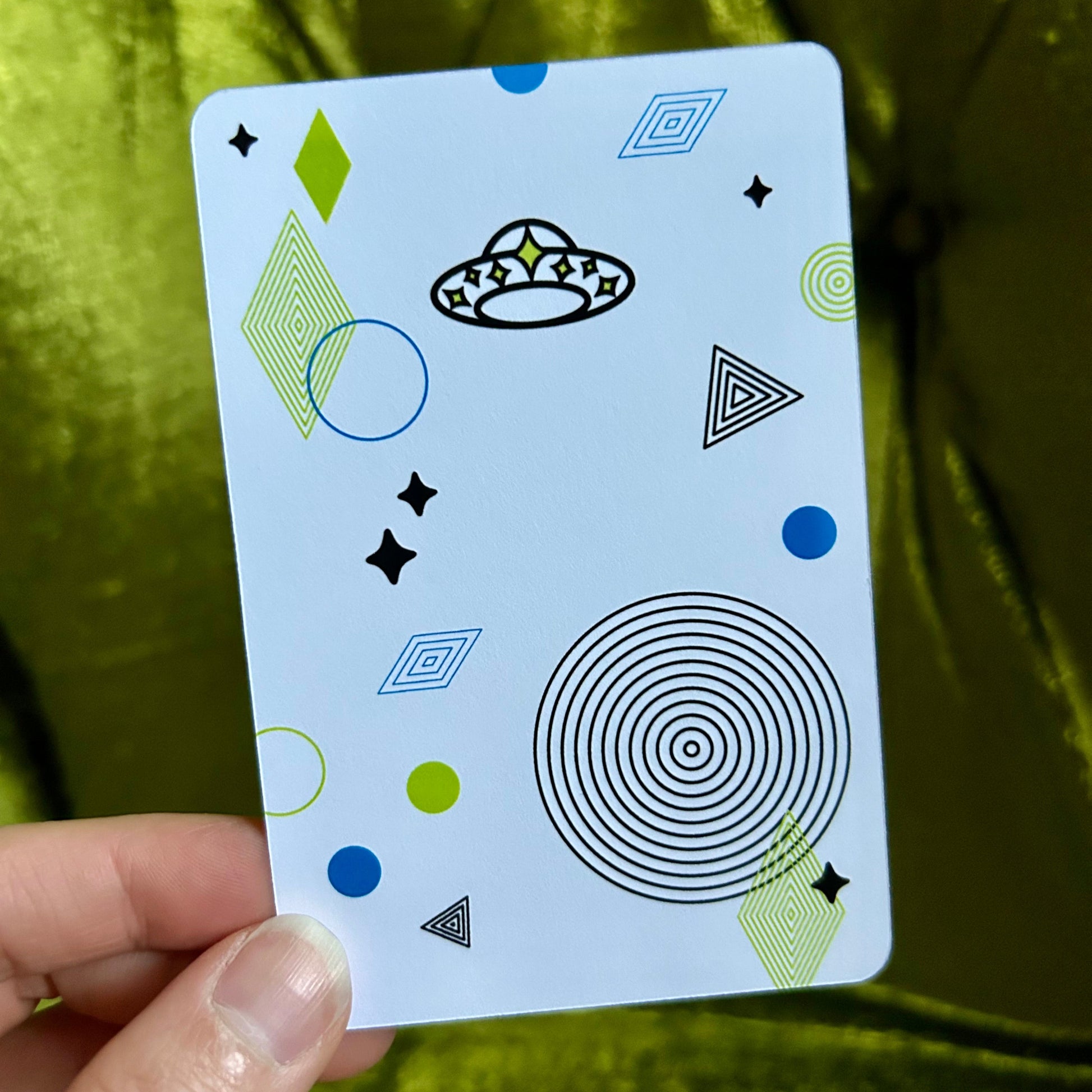 Card with geometric patterns held by a hand against a green fabric background