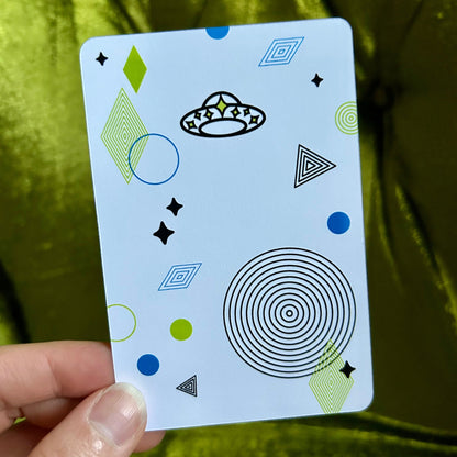 Card with geometric patterns held by a hand against a green fabric background