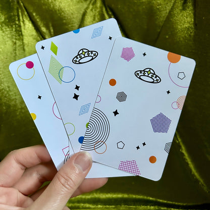 four art prints with geometric designs held by a hand against a green fabric background