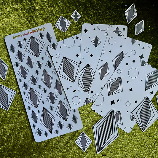 Set of sticker sheets and art prints with geometric designs on a textured green surface