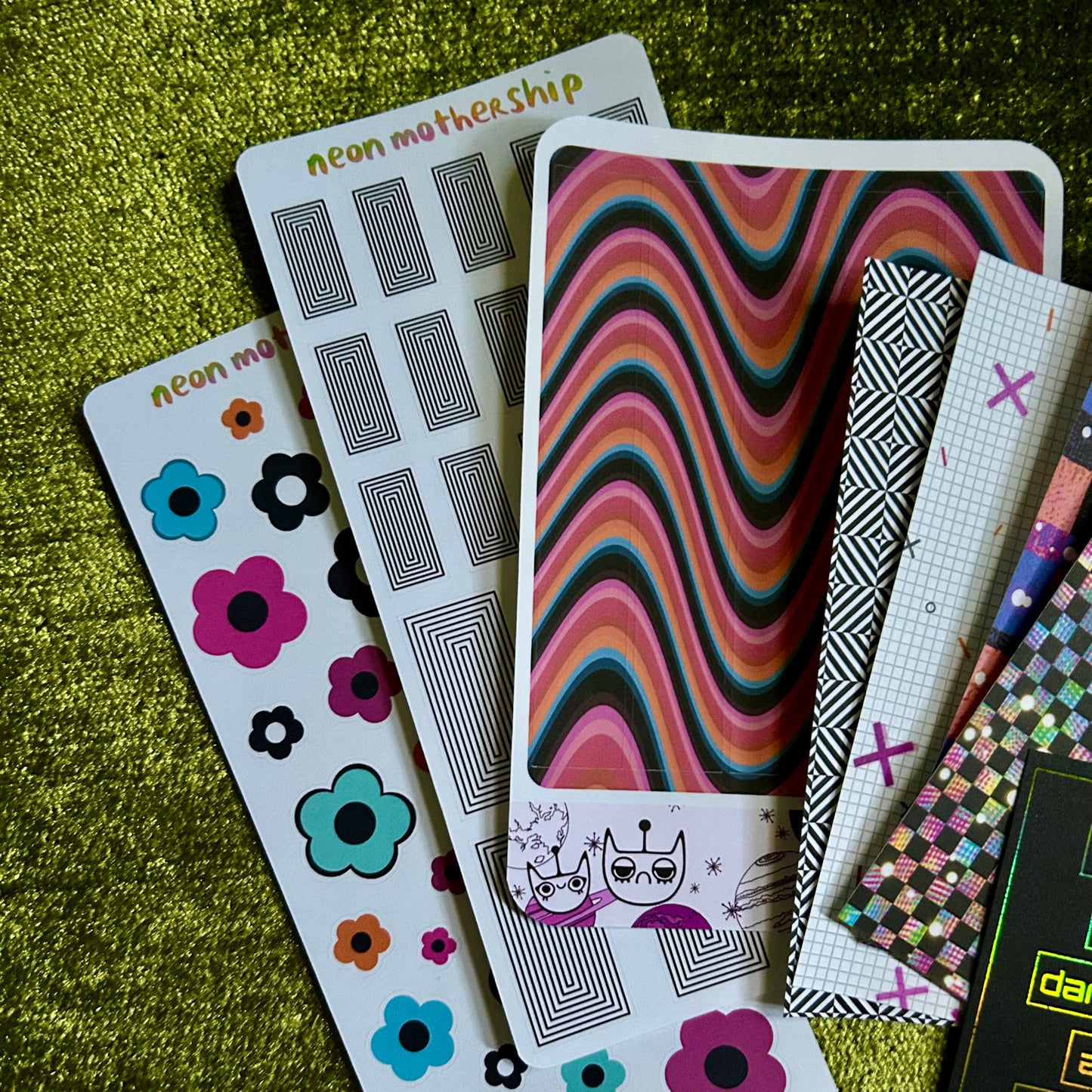 Collection of colorful sticker sheets with various designs on a green textured surface