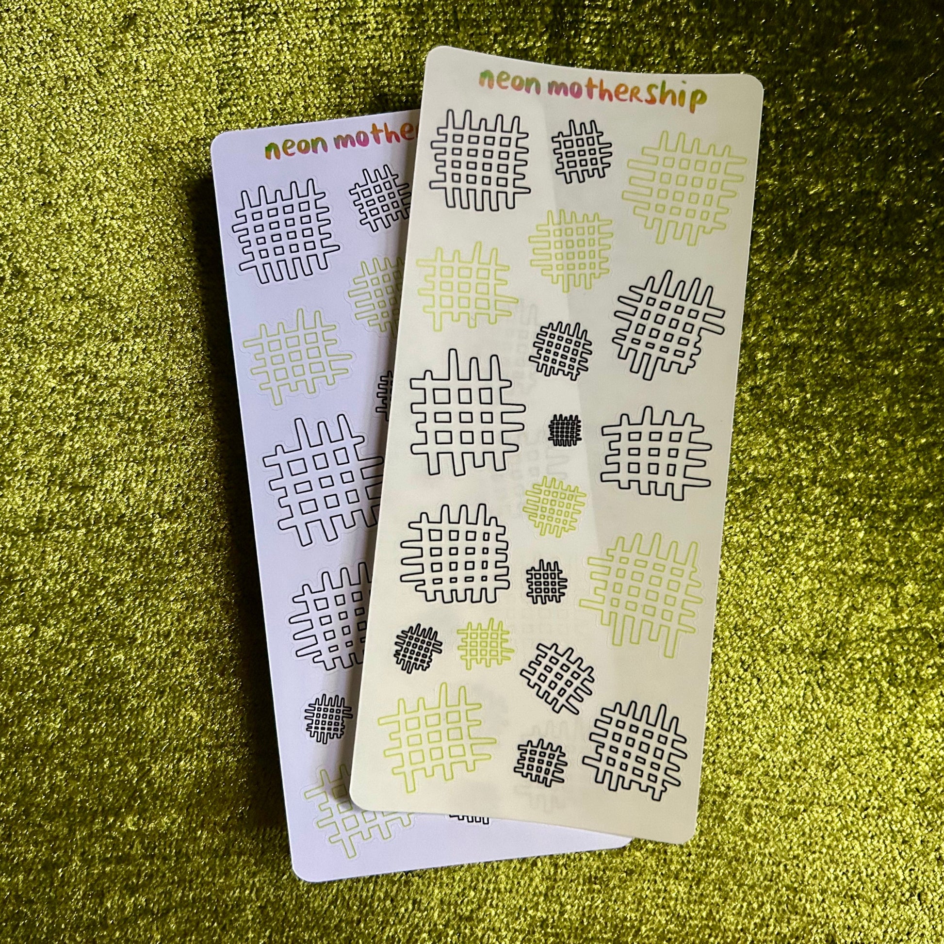 Two small sticker sheets with geometric patterns on a green textured surface