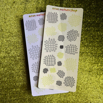 Two small sticker sheets with geometric patterns on a green textured surface