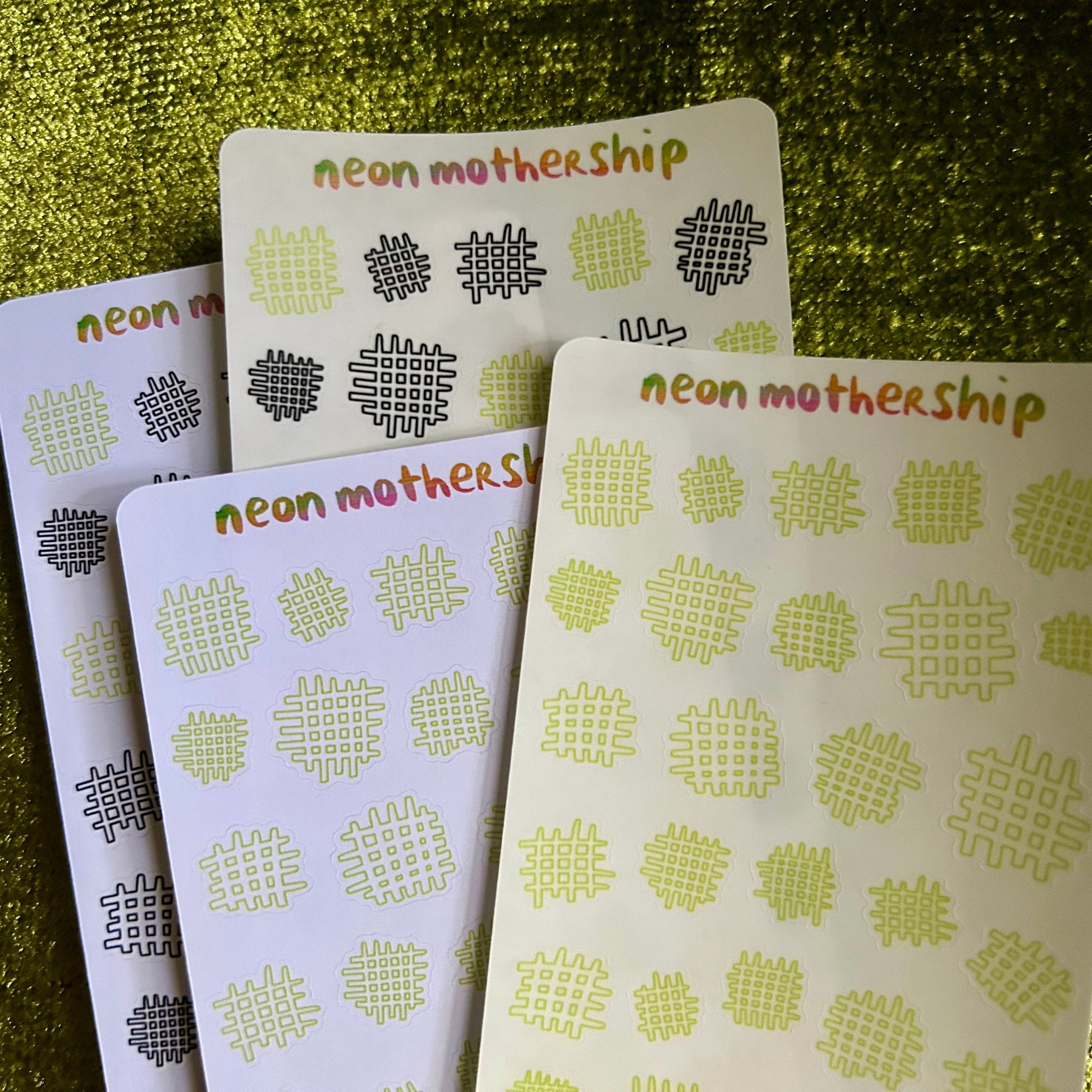 Four sticker sheets with 'neon mothership' text and patterns on a green textured background