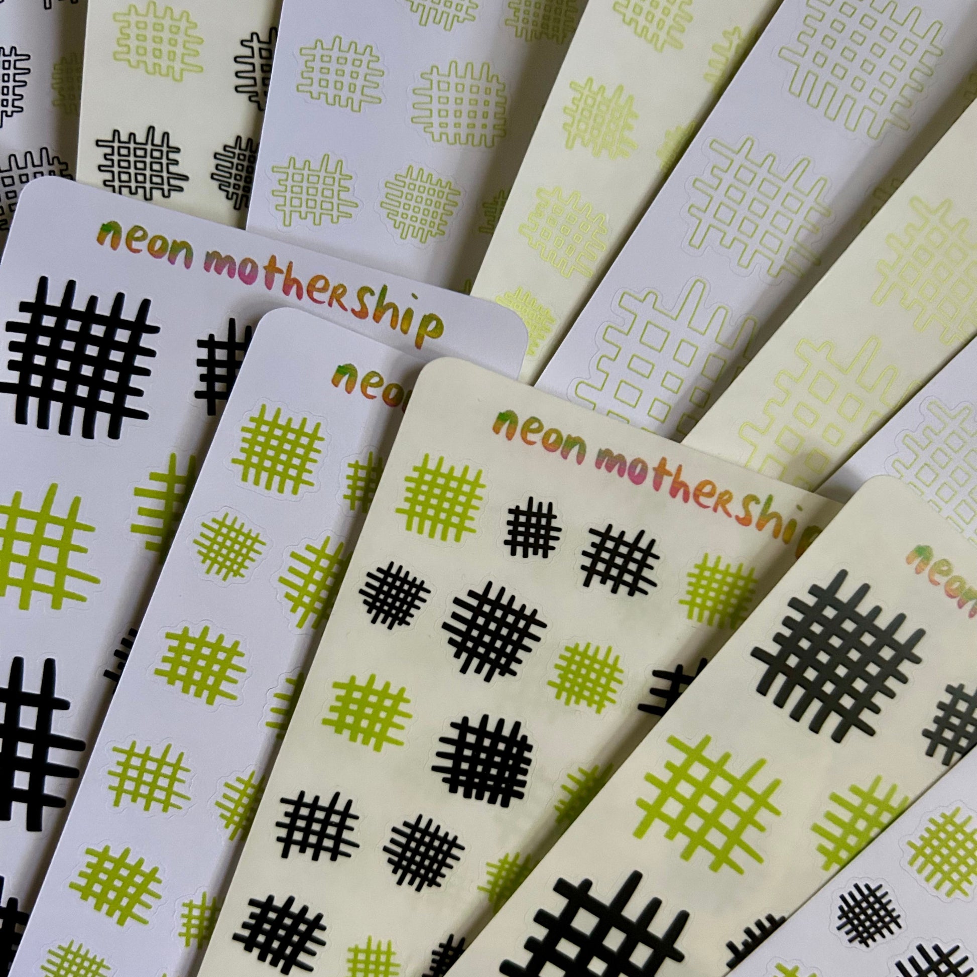 Stack of sticker sheets with geometric patterns and 'neon mothership' branding.