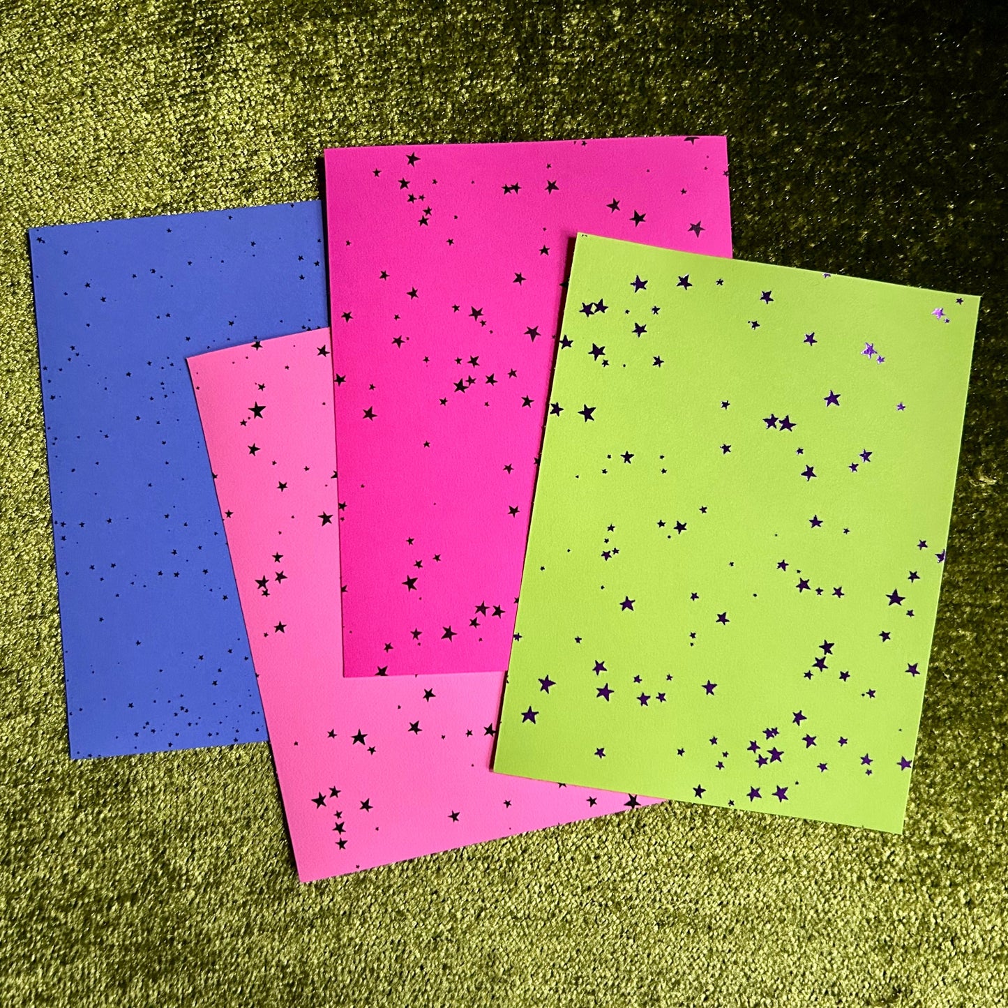 Four sheets of colorful paper with star patterns on a textured green surface