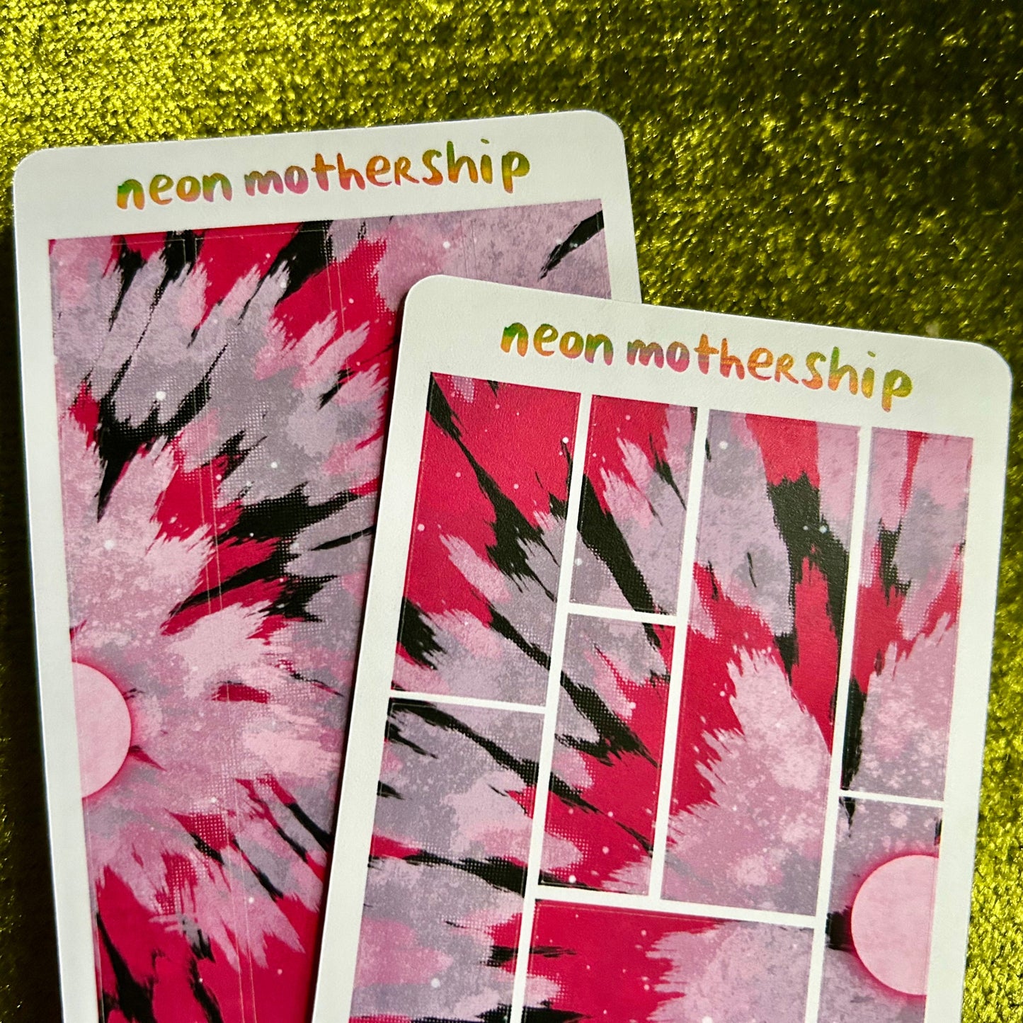 Two sticker sheets with a pink and black abstract tie dye design on a green textured surface.