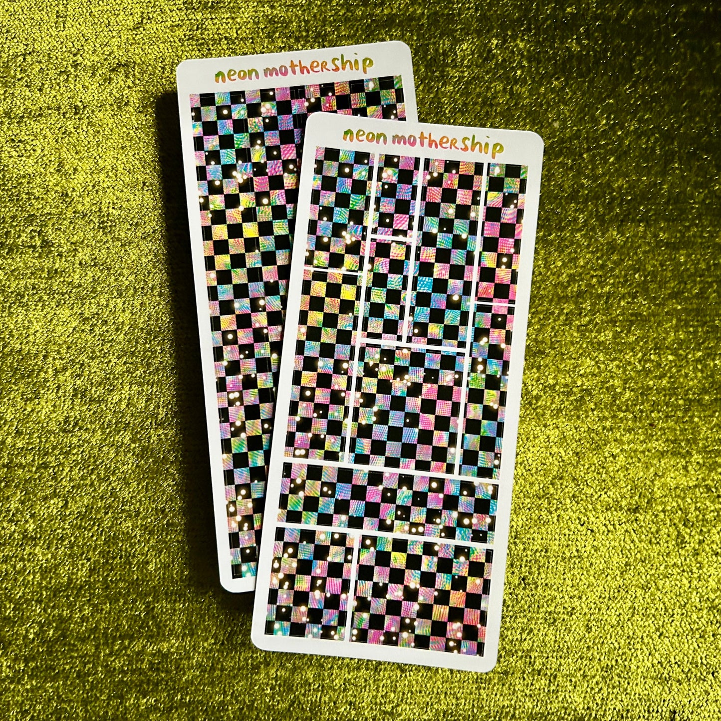 Two sheets of checkered stickers with 'neon mothership' branding on a green textured surface.