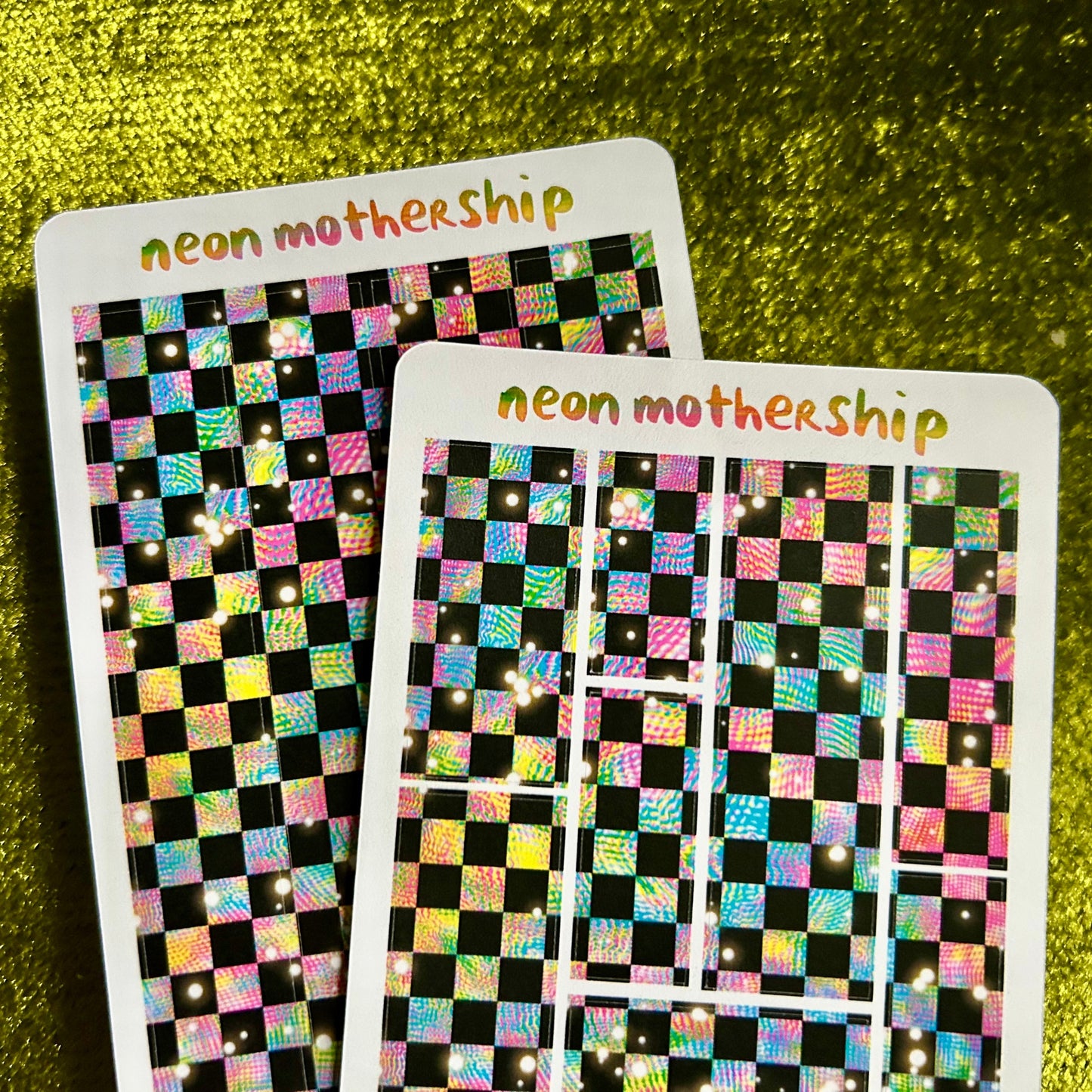 Two sticker sheets with checkered patterns and 'neon motherShip' branding on a green textured background