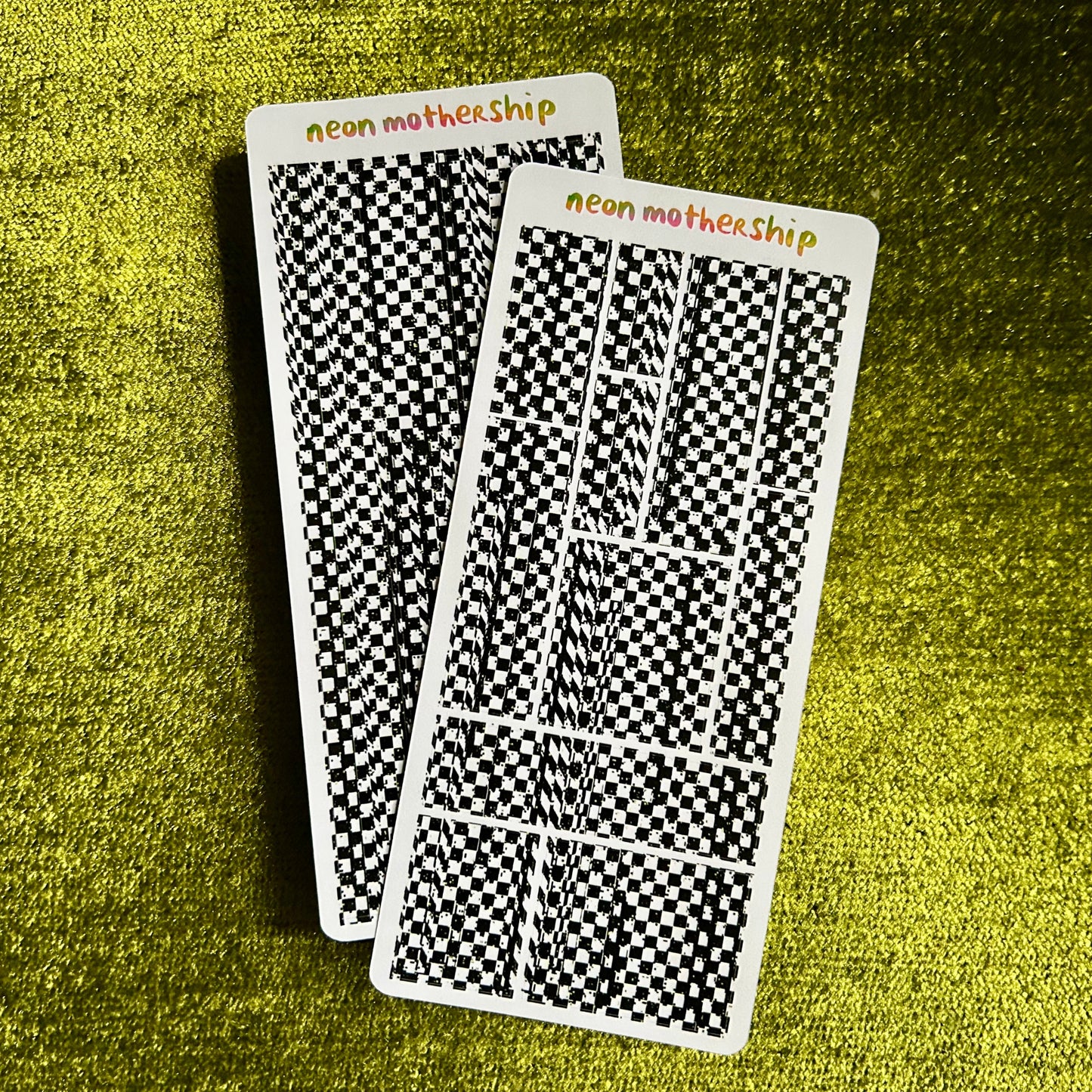 Two checkered sticker sheets with 'neon mothership' branding on a green textured surface