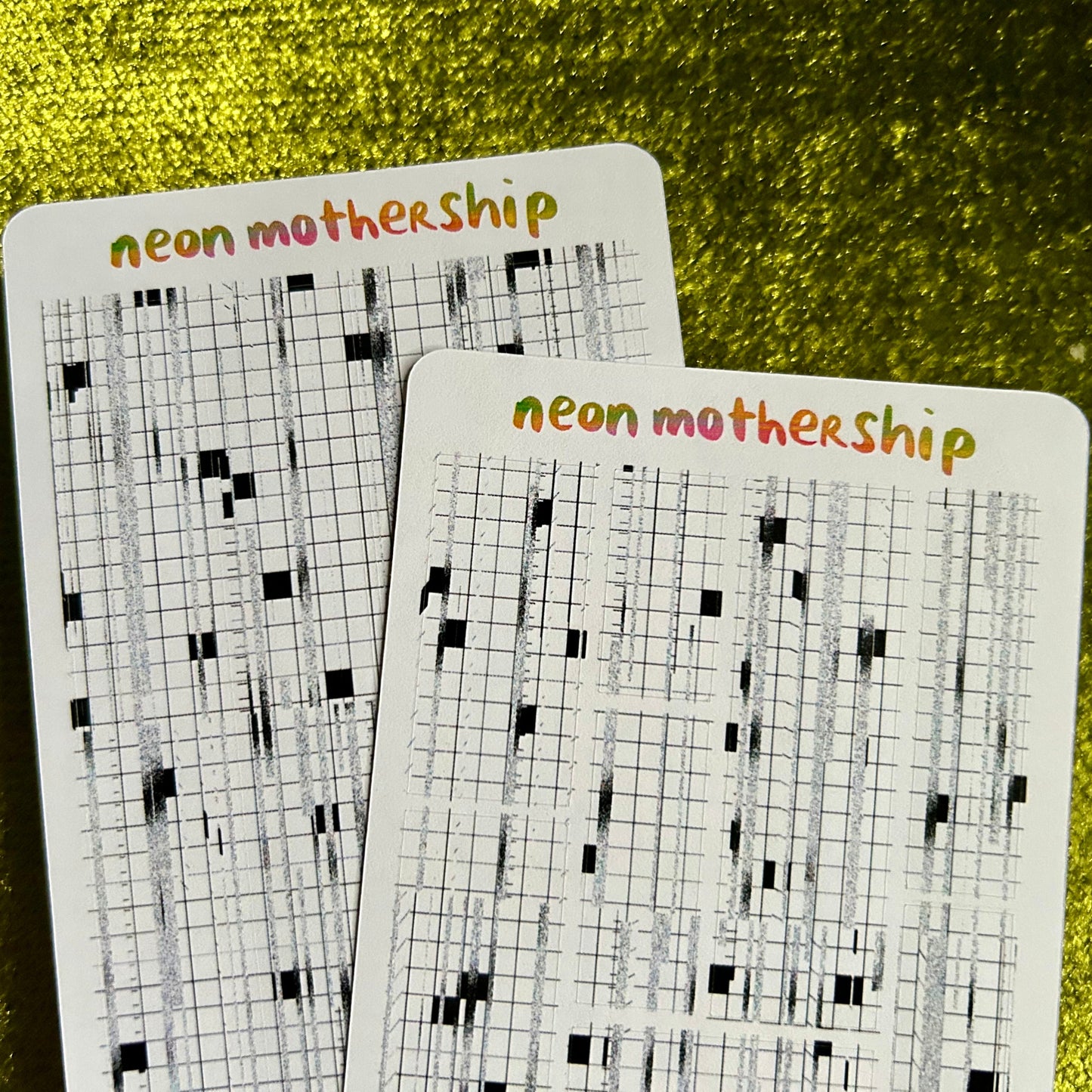 Two sticker sheets with grid patterns and 'neon mothership' text on a green textured background
