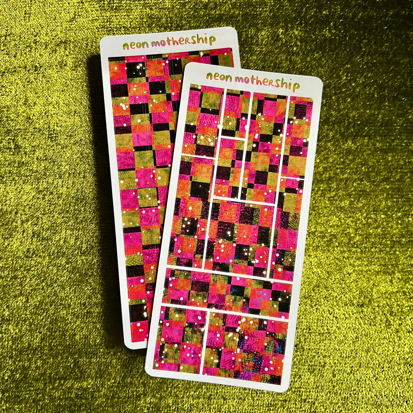 Two colorful sticker sheets with a checkered pattern on a green textured surface.