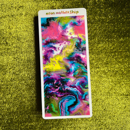 Colorful abstract design on a rectangular card with 'neon mothership' text, placed on a textured green surface.