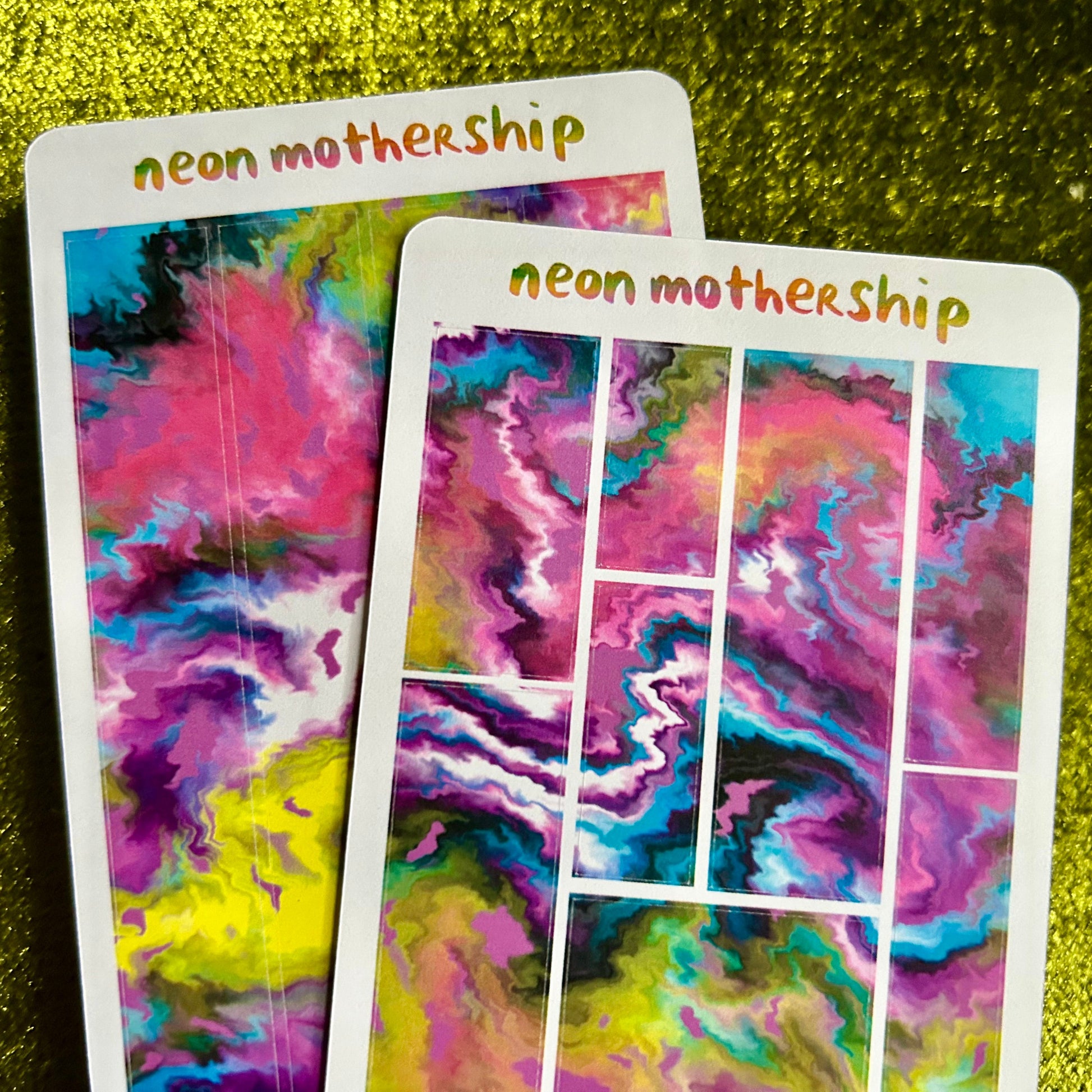 Colorful 'neon mothership' sticker sheets on a green textured surface