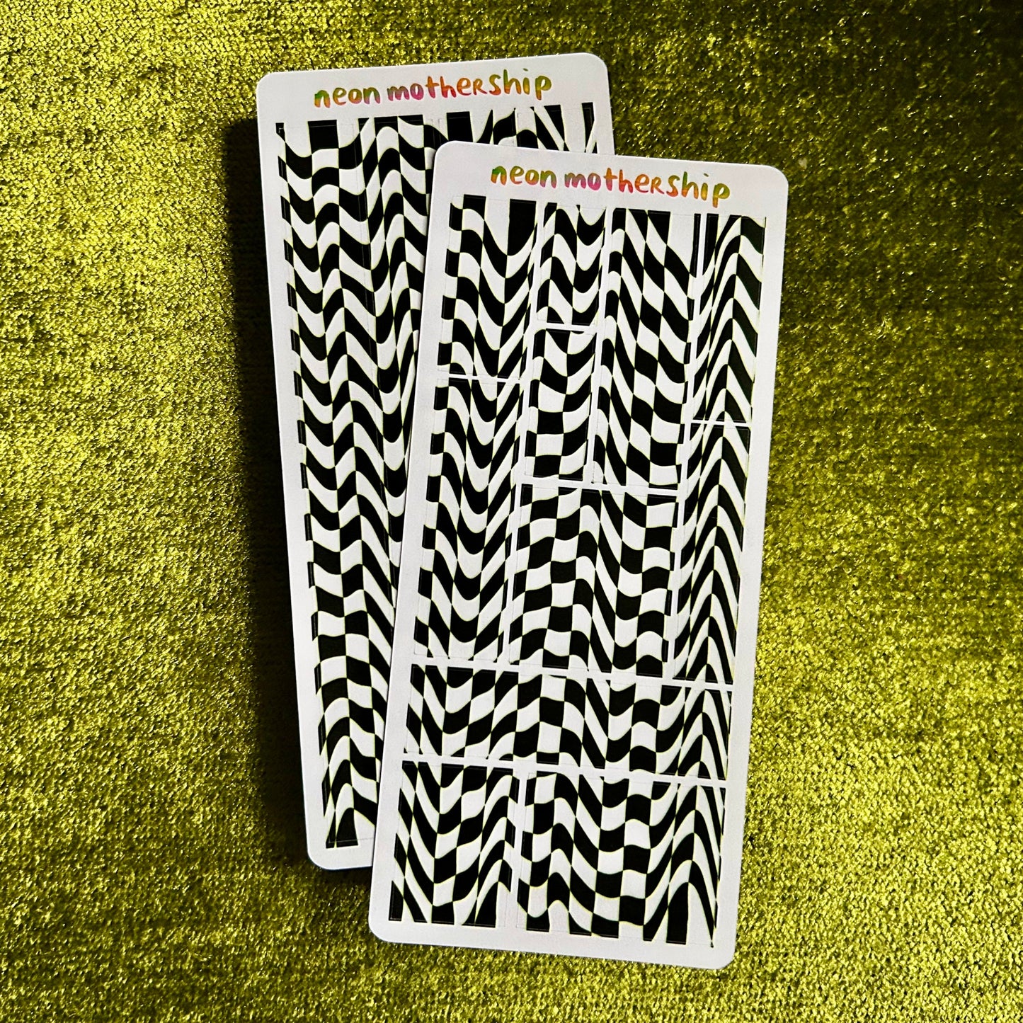 Two sticker sheets with black and white pattern on a green textured surface