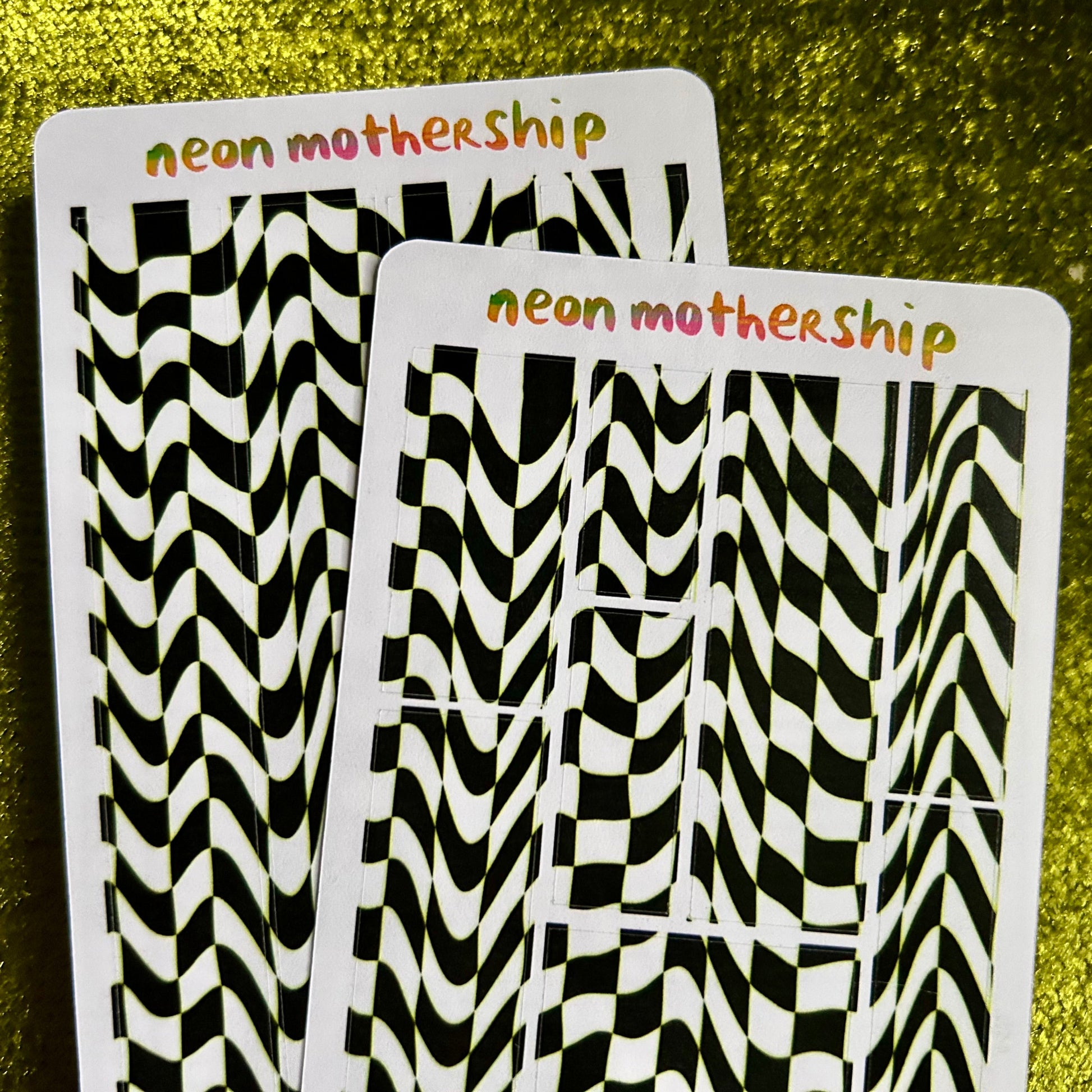 Two sticker sheets with black and white zigzag patterns on a green textured background, labeled 'neon mothership'.