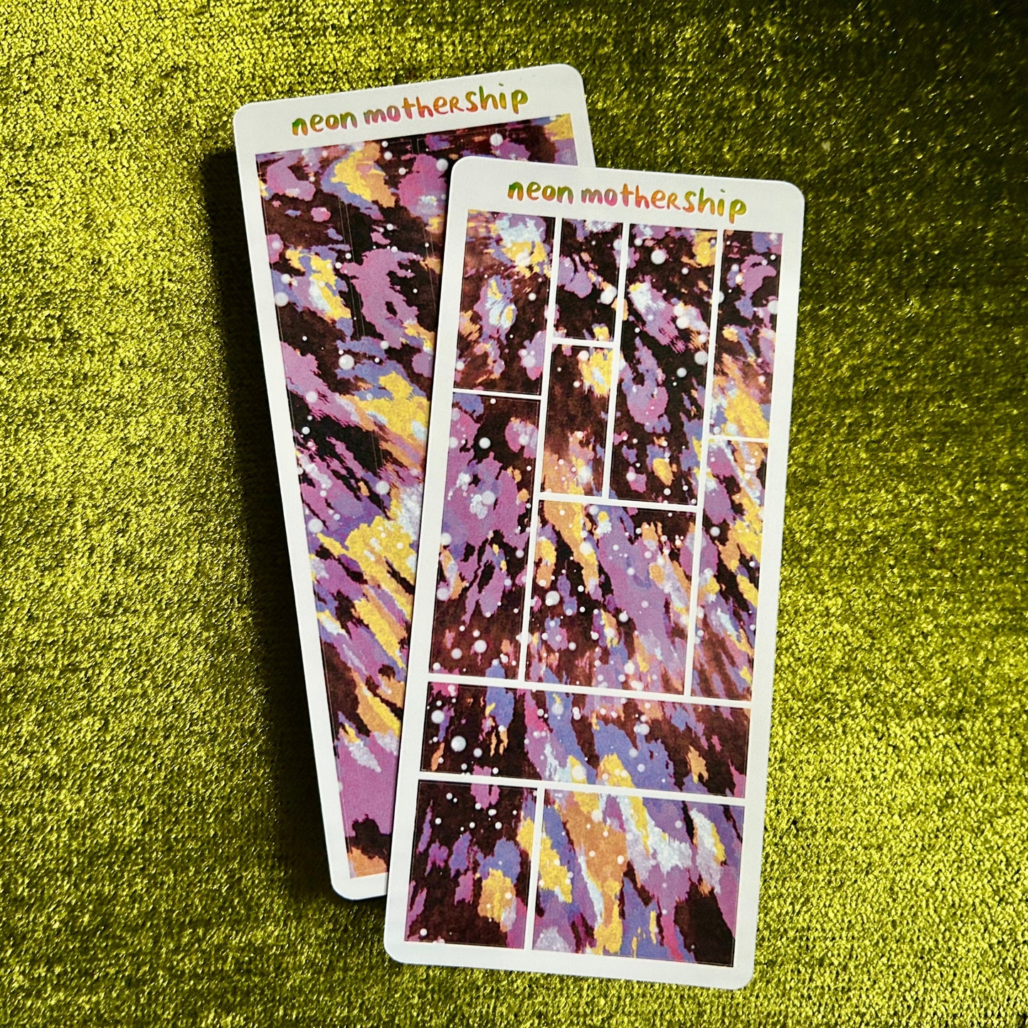 Two colorful sticker sheets with 'neon mothership' text on a green textured surface