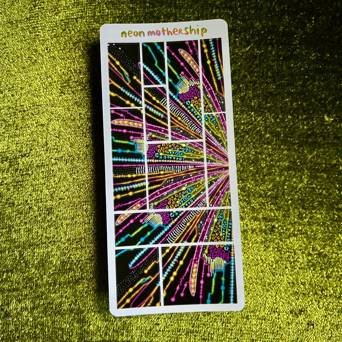 Neon MotherShip sticker sheet on a textured green surface