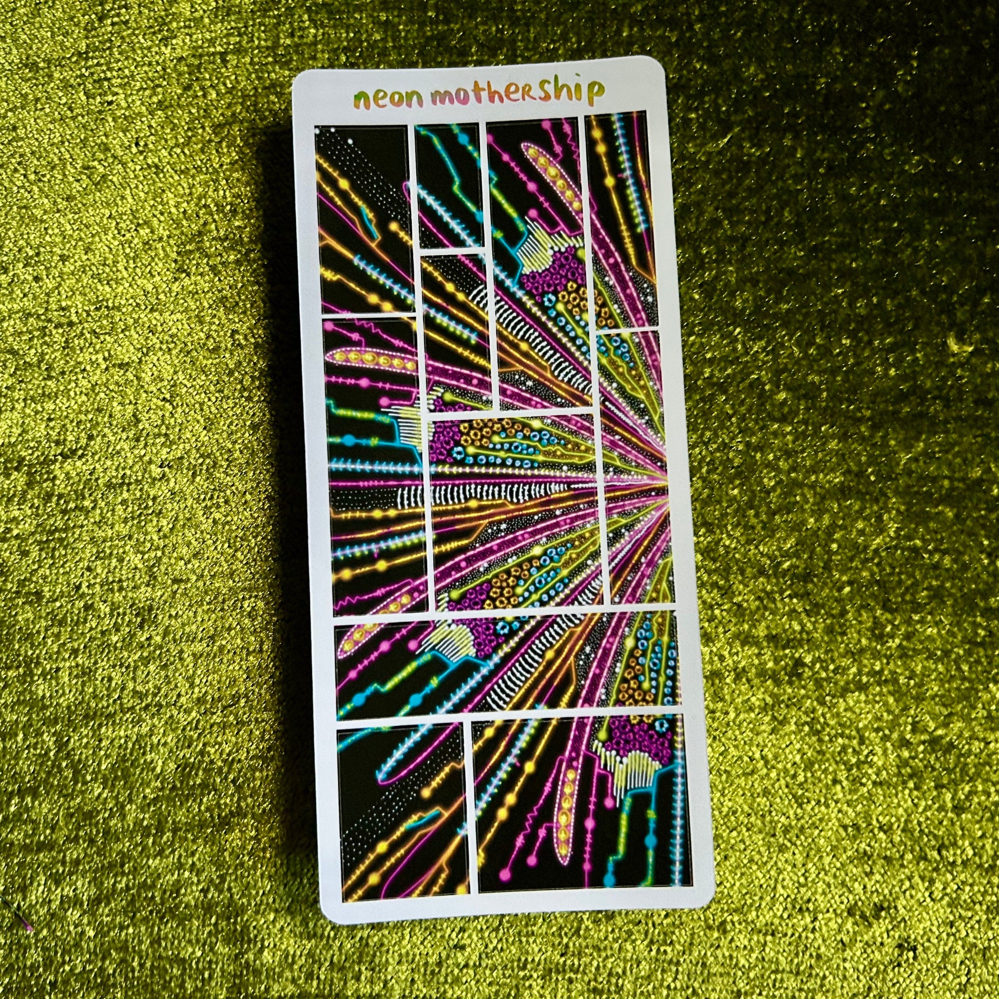 Neon MotherShip sticker sheet on a textured green surface