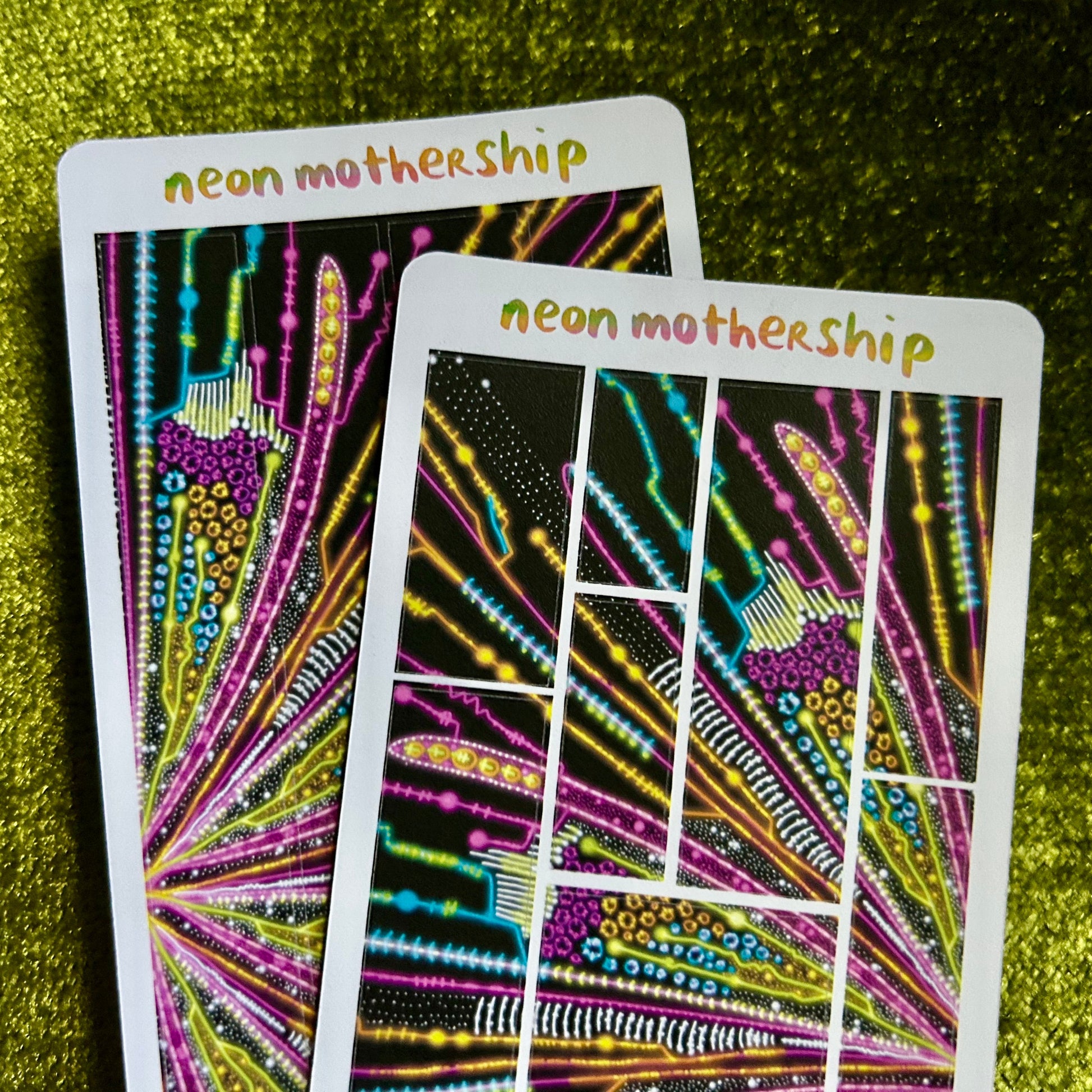 Two colorful 'neon mothership' sticker sheets on a green textured surface