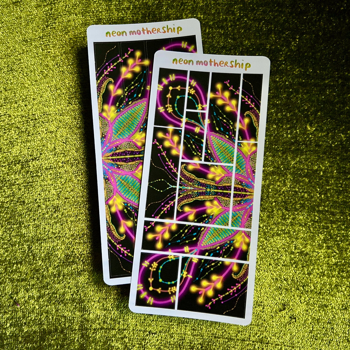 Two bright, glowing neon motherhip sticker sheets on a green textured surface
