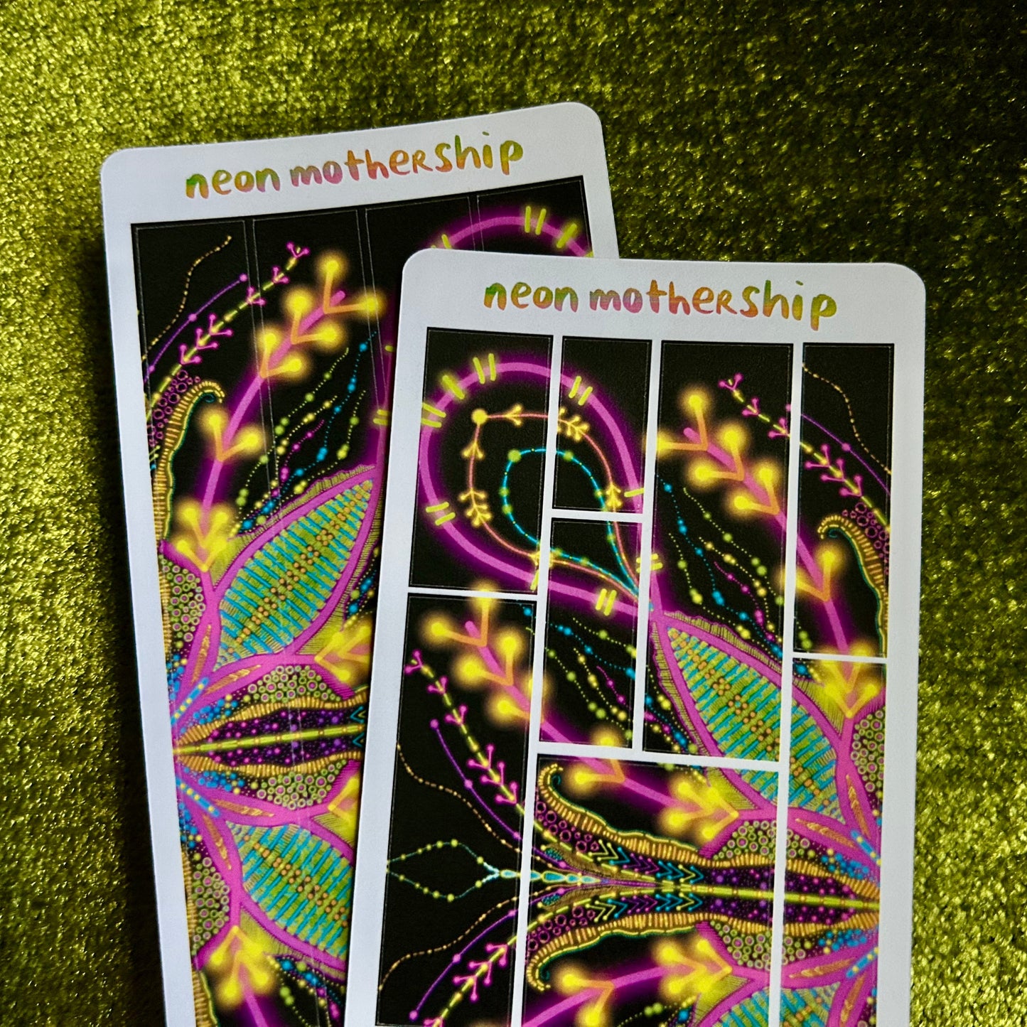 Two neon 'neon mothership' sticker sheets on a green textured surface