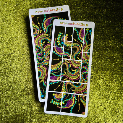 Two colorful sticker sheets with intricate designs on a green textured surface