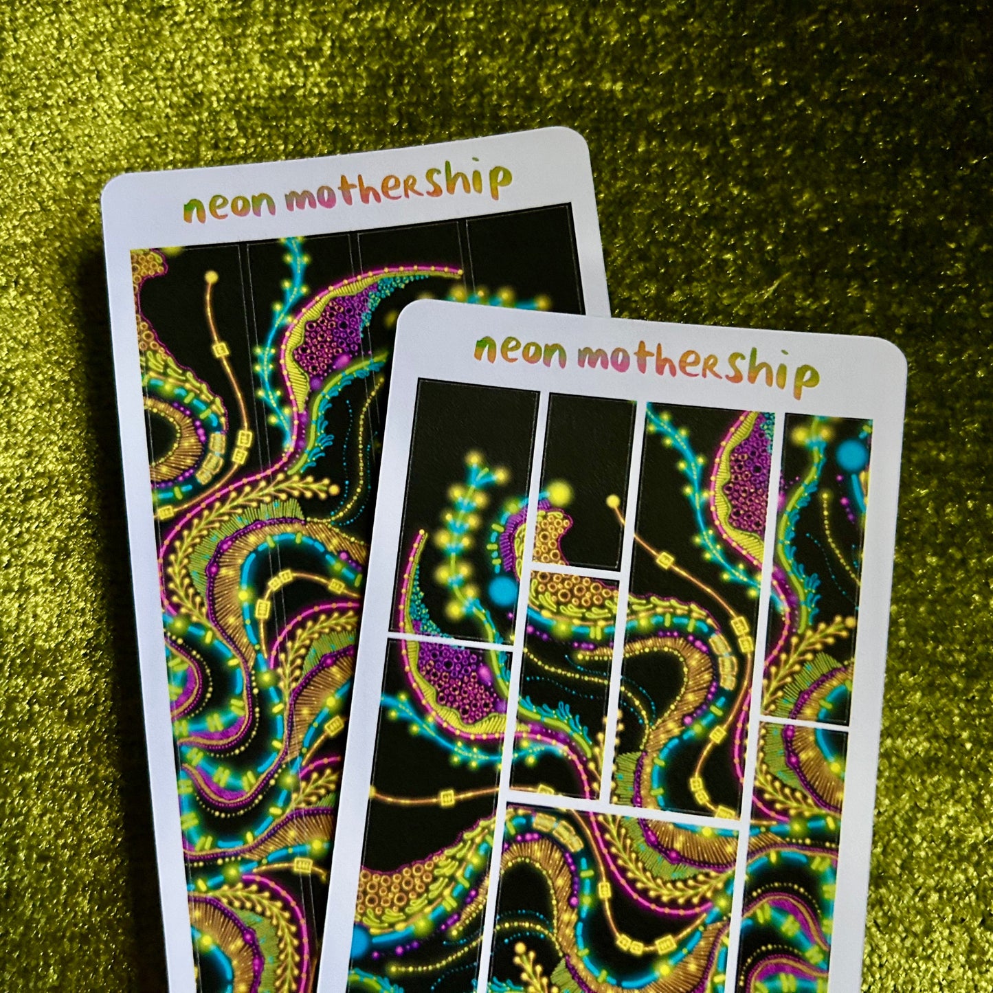 Two neon 'neon mothership' sticker sheets on a green textured surface